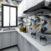 A kitchen featuring white cabinets, a marble backsplash with blue and gold veining, and a black range hood.
