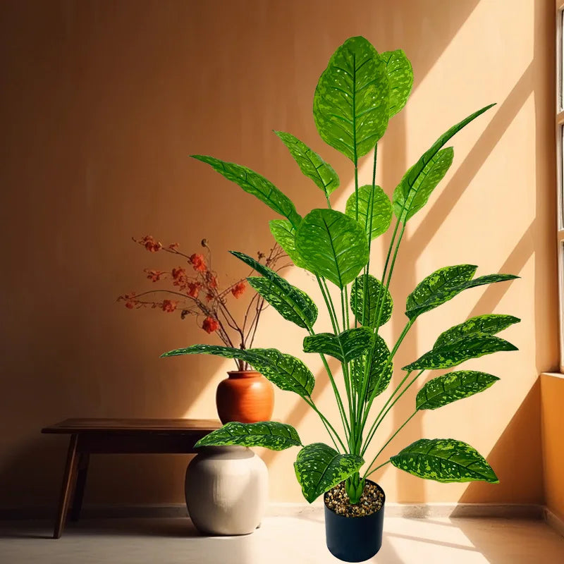 A large artificial tree with lush green leaves stands in a pot on a wooden table next to a window.