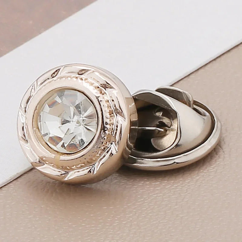 A close-up of a gold-toned pearl and rhinestone no-sew brooch button with a clear stone detail.