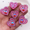 A hand holds a set of twelve heart-shaped pink and orange iridescent resin rhinestone flatbacks.