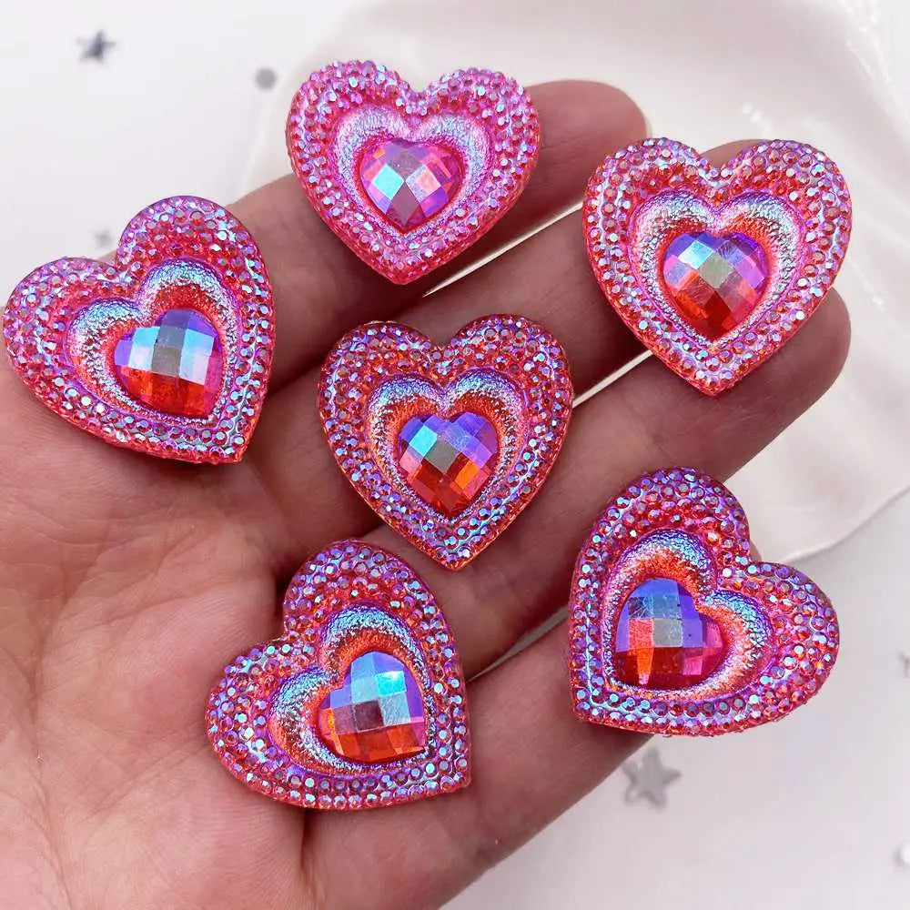 A hand holds a set of twelve heart-shaped pink and orange iridescent resin rhinestone flatbacks.