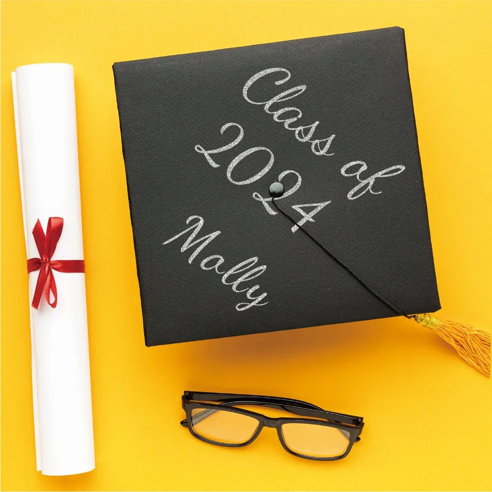 A black graduation card with silver lettering for Class of 2024 and Molly, next to a white rolled paper and black glasses.