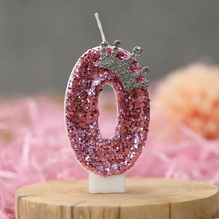 A pink sequin number zero candle with a silver crown topper displayed on a wooden surface.