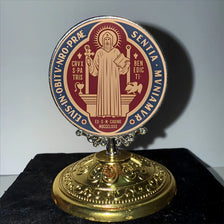 A round, ornate metal ornament with a religious inscription and gold base.