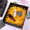 A black box filled with yellow crinkle cut paper shred filler and a gold cosmetic product.