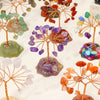 A display of seven chakra healing crystal trees featuring various natural colored stones on wooden branches.