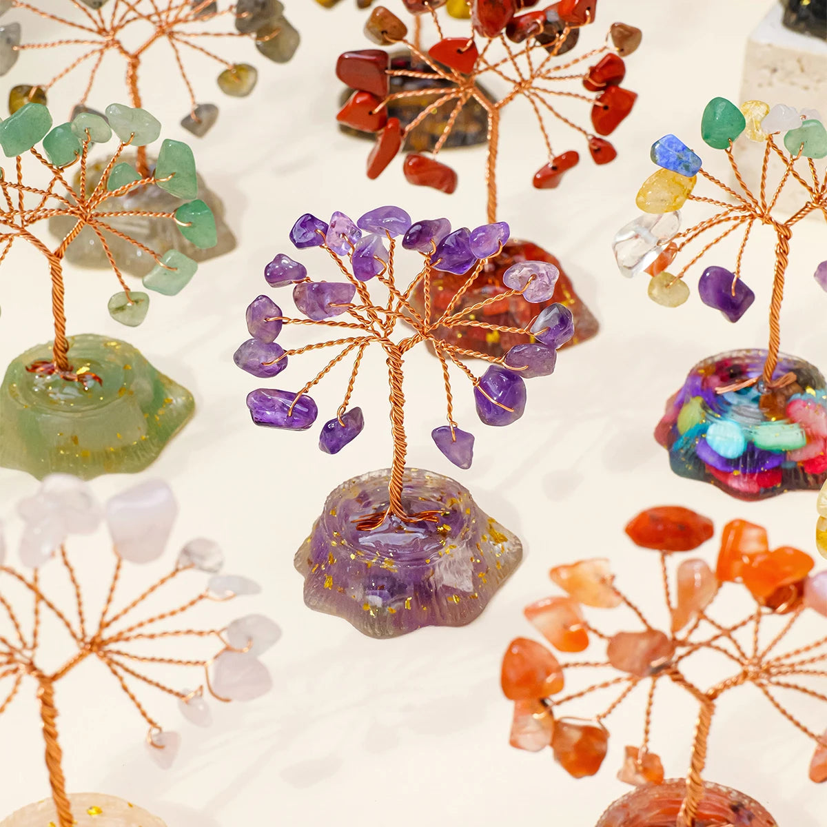 A display of seven chakra healing crystal trees featuring various natural colored stones on wooden branches.