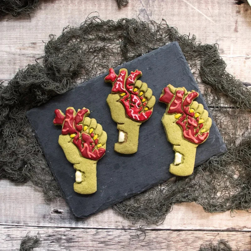 A set of three 3D Halloween cookie cutters and fondant stamps shaped like hands with red and yellow details on a dark slate b
