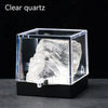 A clear quartz crystal specimen is displayed inside a transparent square box on a dark surface.