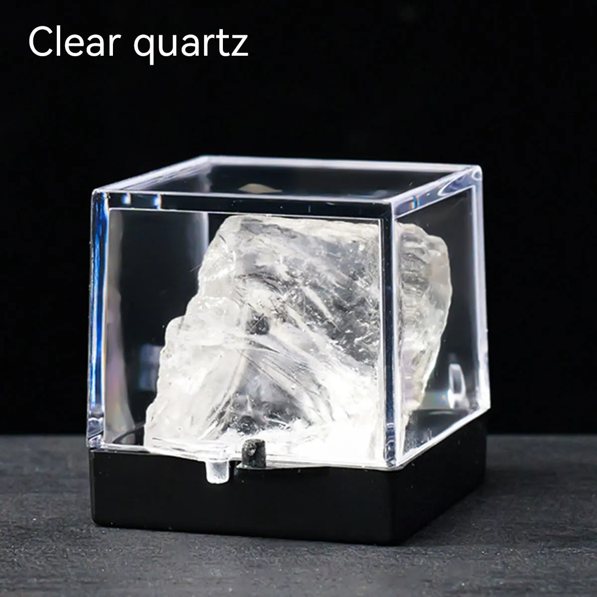 A clear quartz crystal specimen is displayed inside a transparent square box on a dark surface.
