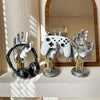 A silver robotic hand and a white game controller are displayed on a shelf next to a black headset.