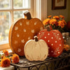 A set of three wooden pumpkin figurines in orange, red, and natural wood are displayed on a dark metal surface.