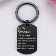 A black keychain with a circular ring attached, featuring text reminders like You are enough and Be kinder to yourself.