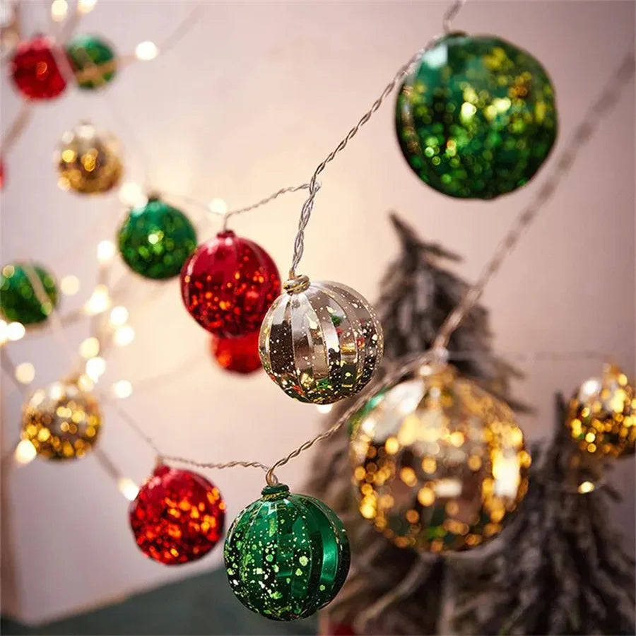 A string of festive LED fairy lights featuring round ornaments in red, green, and gold hanging against a blurred background.