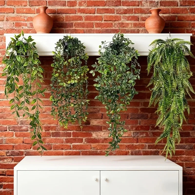 A set of four artificial eucalyptus hanging vines displayed on a white shelf against a brick wall.