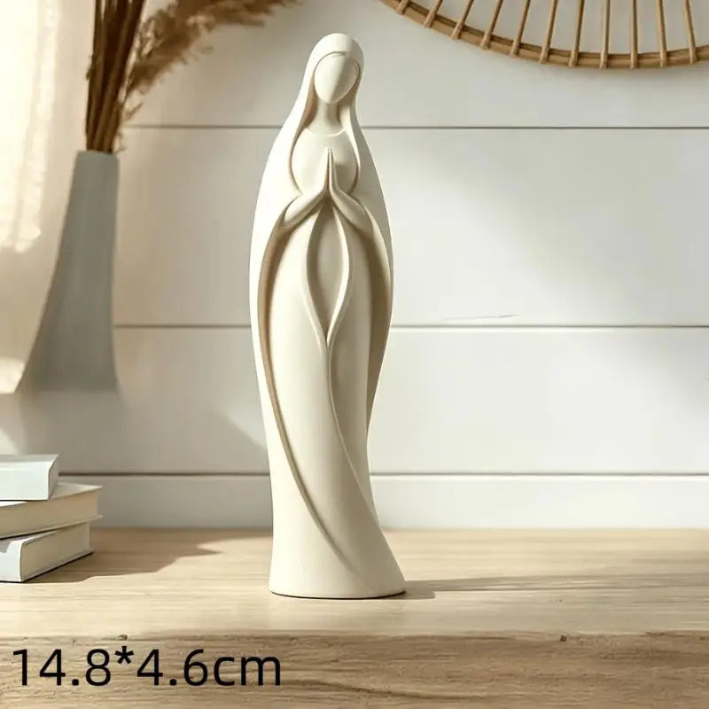 A white gold praying angel figurine statue standing on a wooden surface.