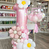 A pink pillar balloon set decorated with white and yellow flowers and stars, including a large number one balloon.