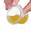 A hand is holding an open clear plastic sauce cup with a lid, showing a yellowish liquid inside.