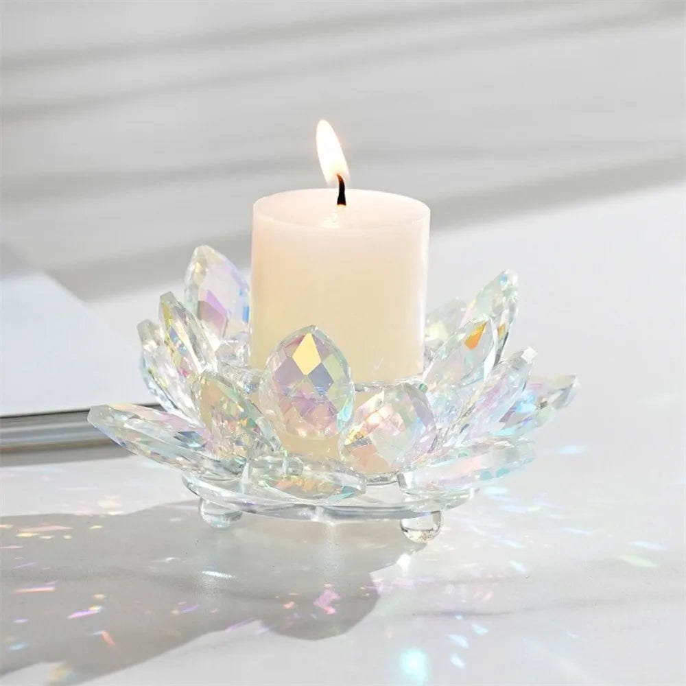 A clear crystal lotus candle holder with a white pillar candle and flame on a white surface.