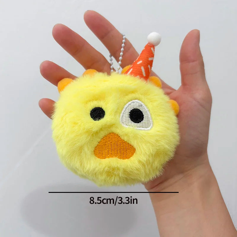 A yellow fluffy plush toy shaped like a face with an orange cone hat being held in a hand.