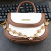A brown and white faux leather bag with a gold chain extender featuring pink rhinestones.