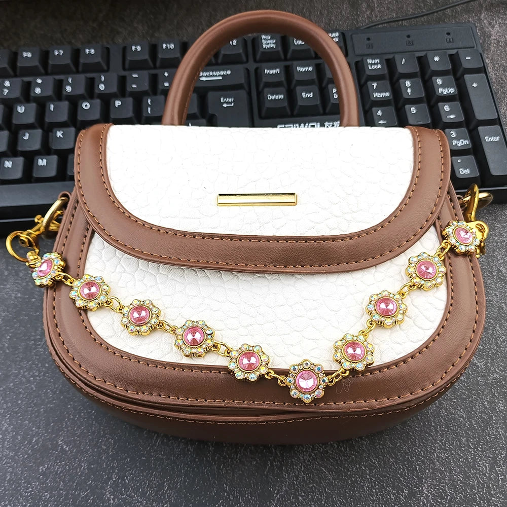 A brown and white faux leather bag with a gold chain extender featuring pink rhinestones.