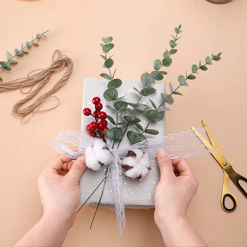 Hands tie a bundle of artificial eucalyptus leaves with white lace ribbon and cotton balls for decor