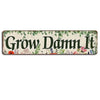 A vintage metal sign with the text Grow Damn It surrounded by green foliage and small flowers on a light background.