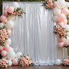A white draped backdrop decorated with pink and peach floral arrangements and clusters of balloons.