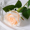 A soft peach colored velvet artificial rose with green leaves on a white plate.