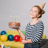 A smiling girl holds a birthday cake with lit candles in front of a yellow couch.