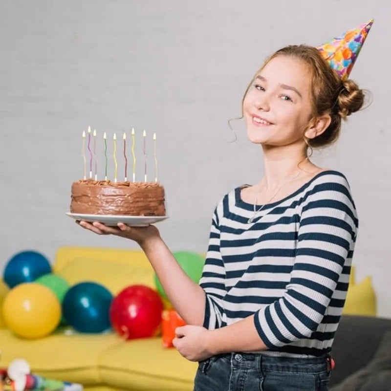 A smiling girl holds a birthday cake with lit candles in front of a yellow couch.