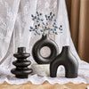 A set of three matte black ceramic vases displayed on a light fabric background.