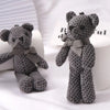 A gray crocheted stuffed bear key pendant sitting on a white surface.