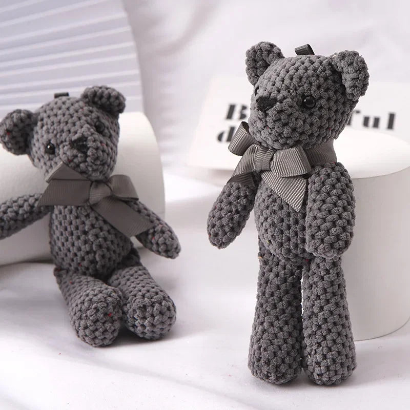 A gray crocheted stuffed bear key pendant sitting on a white surface.