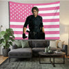 Ein Mann in dunkler Kleidung steht vor einem Tapetenwandbild mit rosa-weiß gestreiften US-Flagge.