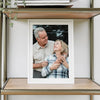 A framed black and white photo of an elderly couple looking at each other, displayed in a wooden shelf unit.