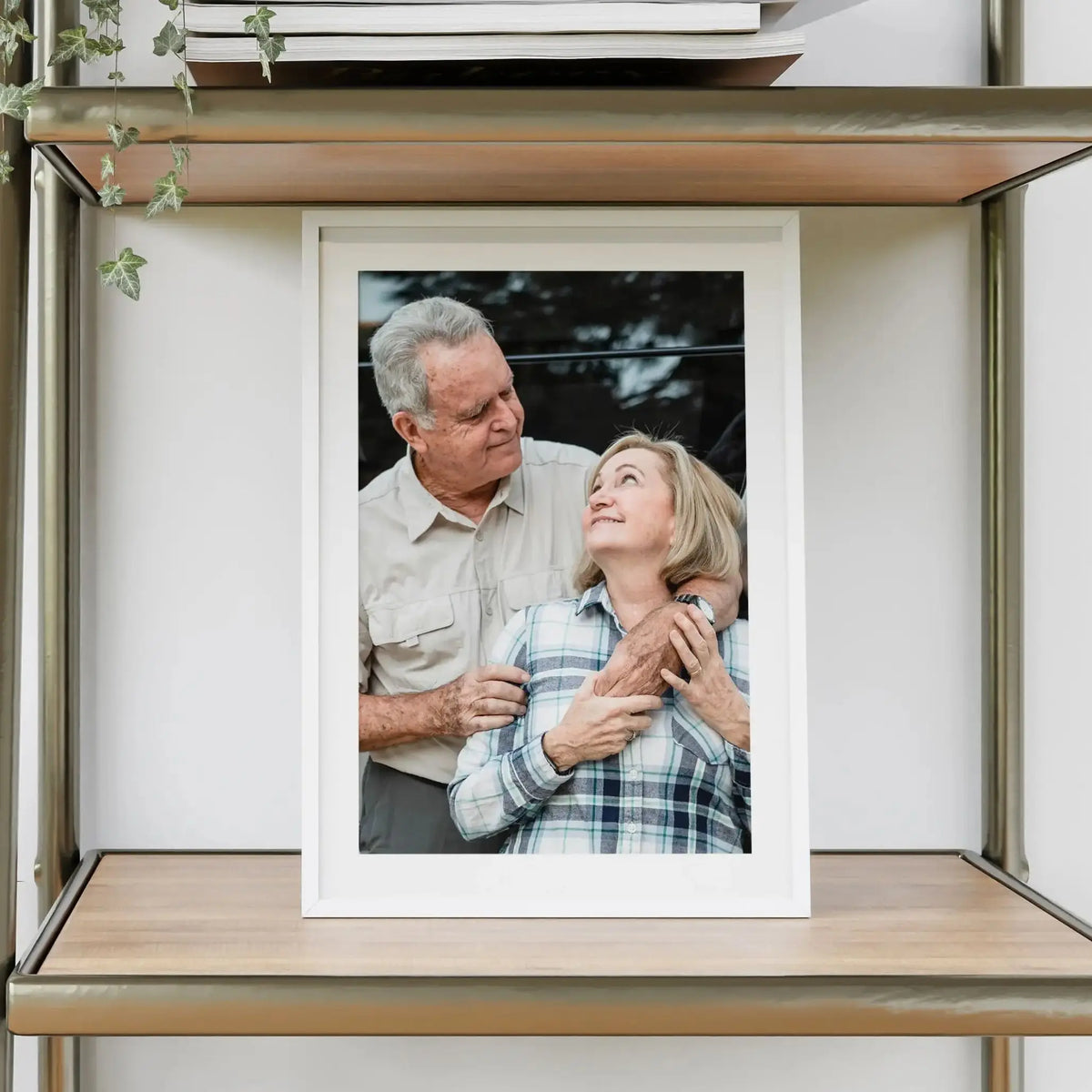 A framed black and white photo of an elderly couple looking at each other, displayed in a wooden shelf unit.
