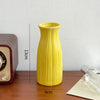 A tall, yellow ceramic bud vase with vertical ridges sits on a wooden surface.