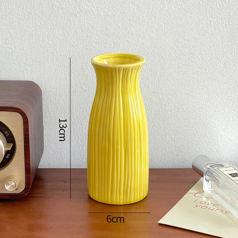A tall, yellow ceramic bud vase with vertical ridges sits on a wooden surface.