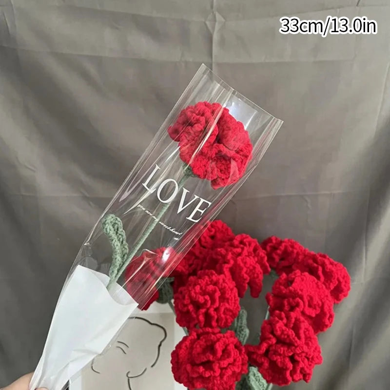 A bouquet of red crochet tulips displayed in a clear plastic sleeve against a gray background.