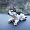 A white and black dog ornament figure with large eyes and a gold chain is placed on a dark surface.
