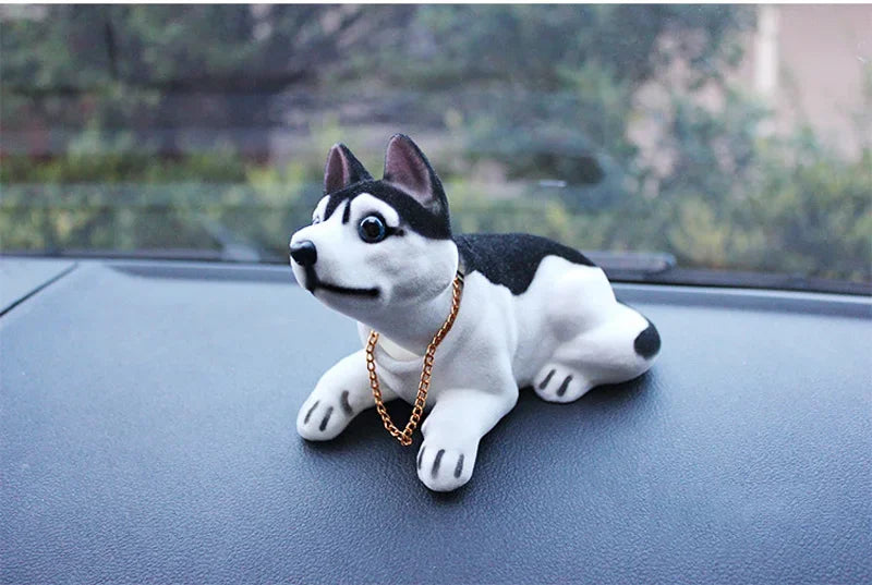 A white and black dog ornament figure with large eyes and a gold chain is placed on a dark surface.
