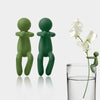 A set of three human-shaped plant supports in a muted green color standing next to a glass of water.