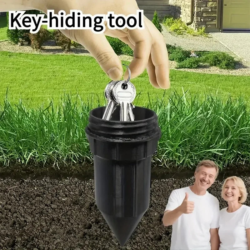 A hand is using a key-hiding tool to place keys into a black plastic container buried in the garden soil.