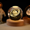 A glass crystal ball night light with a golden glow rests on a wooden base against a dark background.