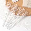 White pearl string beads arranged in a spray on a brown wooden surface with sheer white lace.
