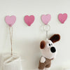 A set of pink heart-shaped adhesive wall hooks with attached key rings displayed against a white wall.