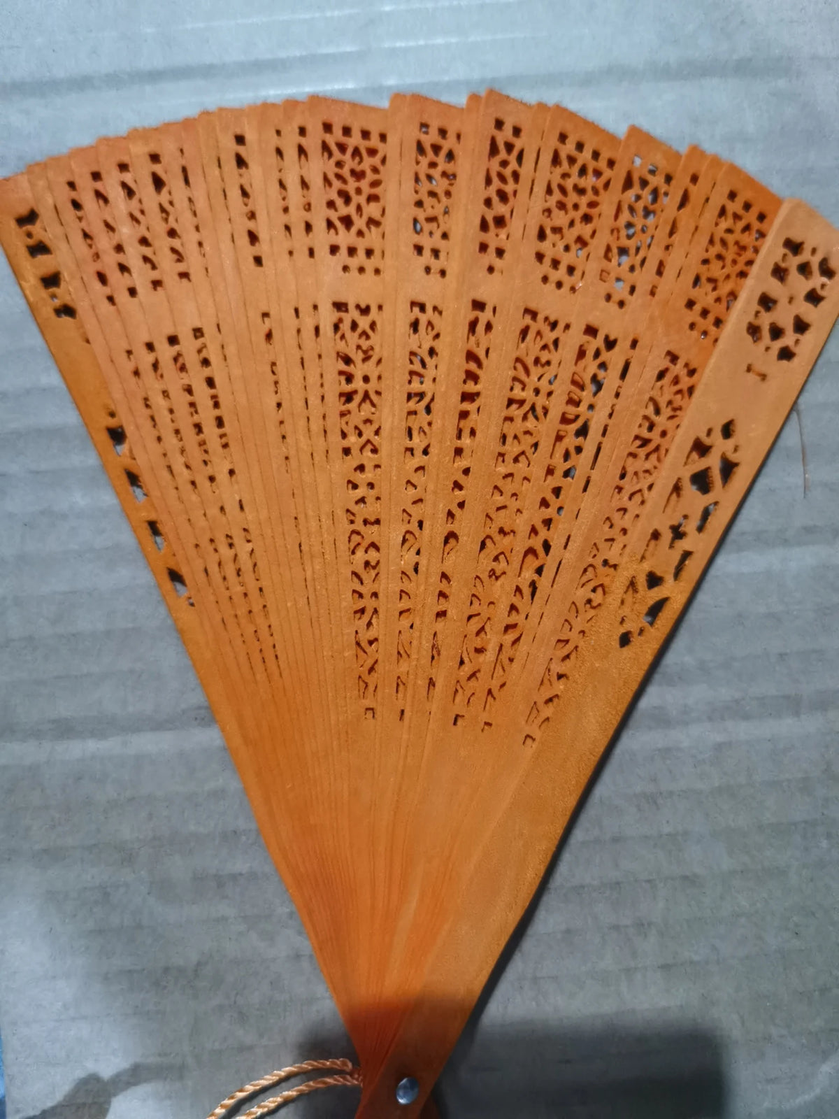 Hand carved bamboo folding fan with intricate cutouts in a warm orange-brown color.
