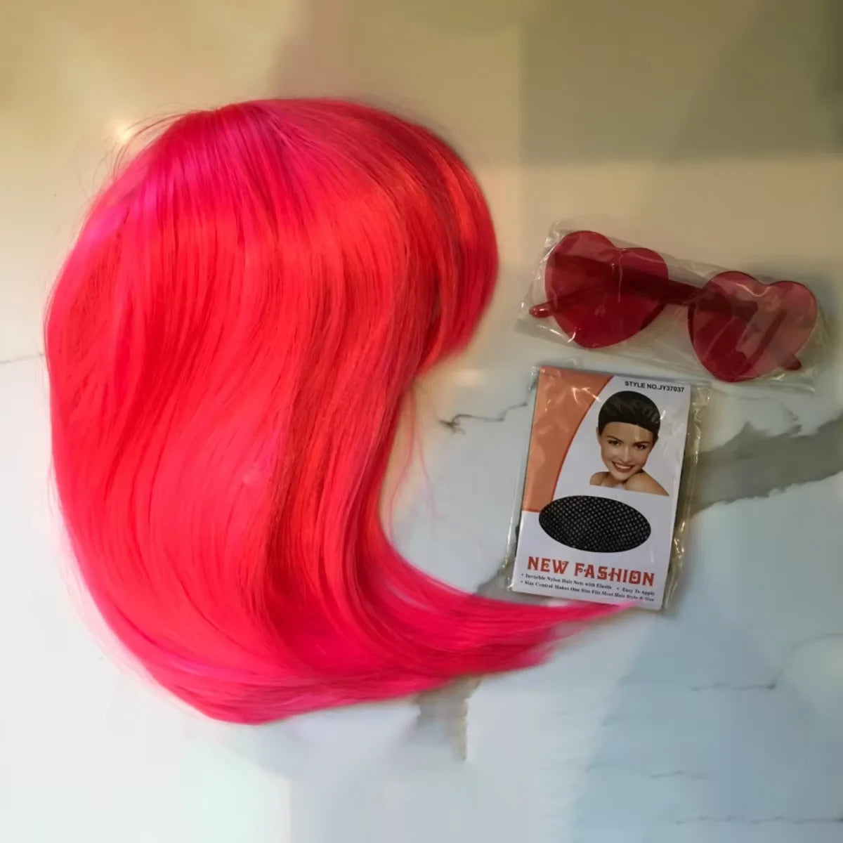 A bright pink long straight hair wig displayed next to a pair of red sunglasses and packaging.